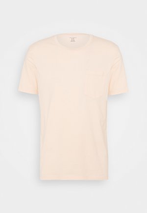 Světlé béžové tričko s krátkým rukávem a kulatým výstřihem, s malou kapsou na levé straně hrudi, zobrazené na jednobarevném bílém pozadí.