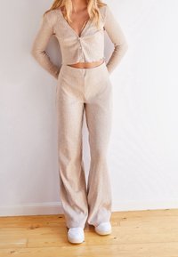 Ljusbeige, ribbad stickad crop top med V-ringning och knappar, ihop med matchande högmidjade vida byxor och vita sneakers.