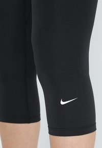 Leggings capri athlétiques noirs en matériau extensible, avec un logo Nike blanc près de l'ourlet et une coupe ajustée.