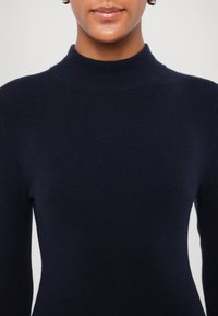 Marineblå ribstrikket turtleneck sweater med lange ærmer, der har en tætsiddende silhuet og sømløs halsdesign. Blød tekstur.