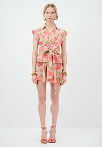 Top a maniche larghe con bottoni a fiori, annodato in vita; abbinato a una mini gonna con motivo coordinato. I materiali sono leggeri e texturizzati.