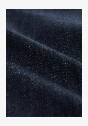 Dunkles Denim-Stoff, das eine glatte Textur mit subtilen weißen Sprenkeln zeigt. Das Material ist gefaltet, wodurch sein Gewicht und seine Dicke zur Geltung kommen.
