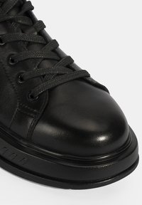 Baskets en cuir noir avec un bout arrondi, un laçage, une surface texturée et une semelle plate en caoutchouc avec de subtils accents horizontaux.