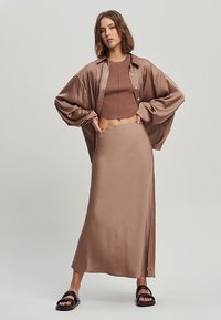 Rjava satenasta oversize srajca preko rjave rebraste crop majice in ustrezne satenaste maksi krila. Črne natikače dopolnjujejo Outfit.