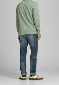 Zielona bluza z białym wzorem w kropki, zestawiona z niebieskimi dżinsami i wielokolorowymi trampkami. Posiada ściągacze na mankietach i u dołu.