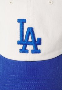 Căciulă de baseball albă cu un logo brodat "LA" de culoare albastră. Dispunând de o visieră albastră și un material texturat cu detalii cusute.