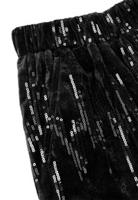 Czarne welurowe spodnie z elastycznym paskiem w talii, ozdobione srebrnymi cekinami ułożonymi w różne pionowe wzory, prezentujące teksturowaną powierzchnię.