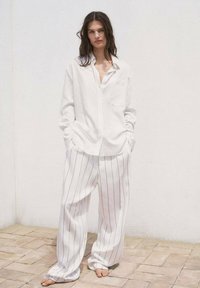 White striped button-up shirt with a front pocket, paired with loose white striped pants, set against a plain white background.