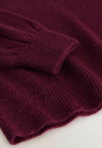 Burgundy sweater featuring a soft, ribbed texture and scalloped hem with matching cuff detail. Fabric appears thick and cozy.