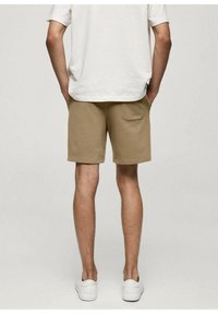 Shorts beiges en matière douce, dotés d'une poche arrière et d'une taille élastique, associés à un t-shirt blanc uni et des baskets blanches.