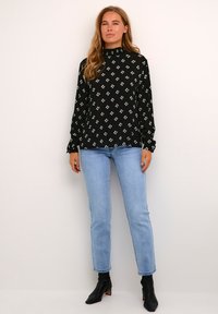 Zwarte blouse met lange mouwen en hoge hals, met een diamantpatroon in wit en blauw. Gecombineerd met lichtblauwe skinny jeans en zwarte enkellaarsjes.