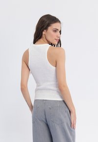 Top de tirantes blanco acanalado con un diseño ajustado, tirantes anchos y un escote redondeado, combinado con unos pantalones vaqueros de tiro alto de color gris claro.