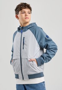 Kevyt hupparitakki harmaassa ja sinisessä, jossa on vetoketjullinen rintatasku, elastiset hihansuut ja rento malli. Sileä rakenne, jossa on kontrastivärisiä yksityiskohtia.