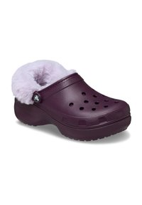 Fioletowe klompy z puszystym liliowym wykończeniem, z wentylacyjnymi otworami i teksturowaną podeszwą dla lepszej przyczepności. Akcentowane okrągłym logo z boku.