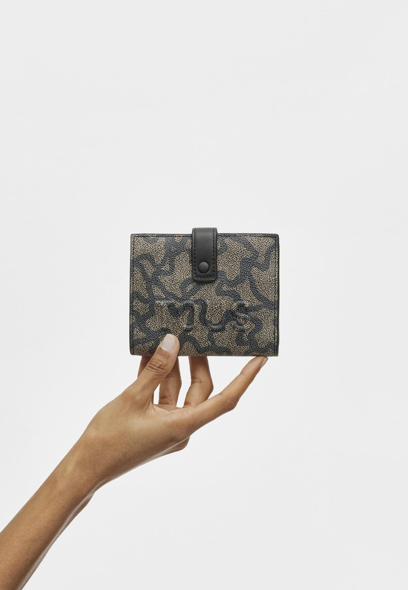 Portefeuille noir et beige avec un motif texturé, doté d'une fermeture à bouton pression noire. Forme carrée compacte, tenu entre les doigts.