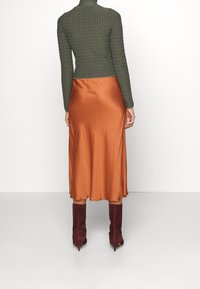 Gebreide groene top met een getextureerd ontwerp, gecombineerd met een satijnen oranje midirok, afgewerkt met bordeauxkleurige laarzen met hak.