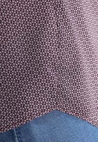 Mönstrad tyg i mörk lila med vitt blommönster, kombinerat med ljusblå denim. Märkbar texturkontrast mellan materialen.