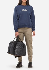 Sac de sport gris avec des sangles noires et le logo "Millet", sweat-shirt bleu marine avec un logo blanc, pantalon cargo beige et chaussures foncées.