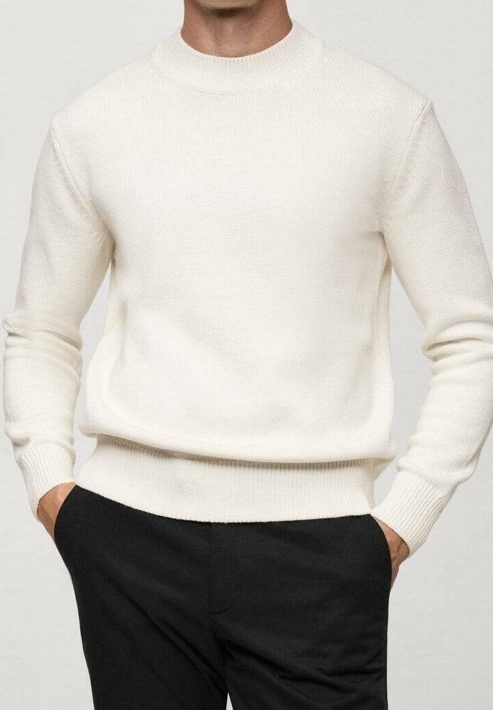 Homme portant un pull en maille de couleur crème à manches longues et un pantalon noir, les mains posées négligemment dans les poches, sur un fond neutre.