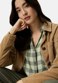 Braune Cordjacke über einem grün-grau karierten Hemd. Besondere Merkmale sind Knöpfe, sichtbare Nähte und gerippte Textur.