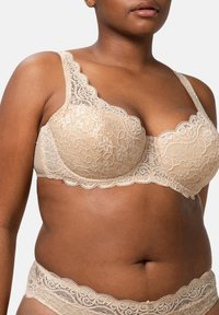 Beige pitsikoristeinen rintaliivi, jossa on aaltoileva reuna, tuki alumiinipannan avulla ja satiininen viimeistely. Mukana samansuuntaiset pitsialushousut, joissa on samanlaisia yksityiskohtia.