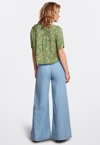 Grünes, floral bedrucktes Kurzarmoberteil mit einem cropped Design, kombiniert mit hochgeschnittenen, hellblauen, weiten Jeans. Strukturierter Stoff mit lässigem Schnitt.