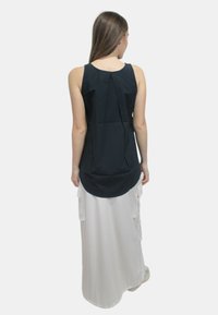 Canotta blu navy senza maniche con una vestibilità rilassata, caratterizzata da un dettaglio arricciato sul retro. Abbinata a una lunga gonna bianca con tasche laterali.
