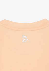 Tissu de couleur pêche claire avec un col rond côtelé et un petit logo abstrait blanc centré sous le col.