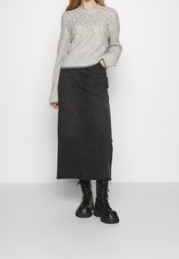 Grauer Strickpullover mit strukturierter Musterung, kombiniert mit einem schwarzen Denim-Maxirock mit geradem Schnitt und rohem Saum. Schwarze Schnürstiefel.