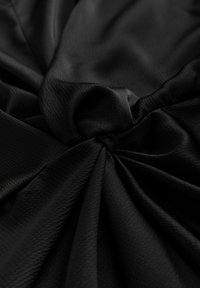 Fekete szövet struktúrált felülettel, gyűjtött és csavart részekkel, amelyek kiemelik a sima és folyamatos redőzést.