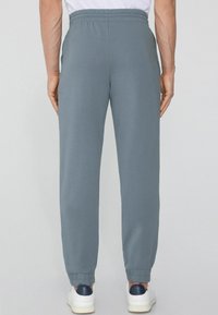 Szare, zwężane dresy wykonane z miękkiego materiału z elastycznym paskiem w talii i ściągaczami. W połączeniu z białymi sneakersami z granatowymi akcentami.