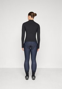 Černé top s dlouhým rukávem, přiléhavé tmavě modré legíny s polstrovanou částí, elegantní design a hladká textura, nošeno s cyklistickými botami a tmavými ponožkami.