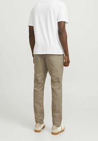 Béžové bavlněné kalhoty s úzkým střihem, zdobené zadními kapsami, nošené s bílým tričkem a světlými teniskami.