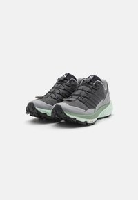 Scarpe da trail running leggere in grigio e nero con suola testurizzata, lacci elastici e intersuola verde menta per stabilità e aderenza.