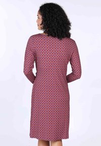 Langärmeliges Kleid aus pinkem Stoff mit einem gemusterten Design aus wirbelnden Formen in Lila und Gold, figurbetonte Silhouette, knielanger Saum.