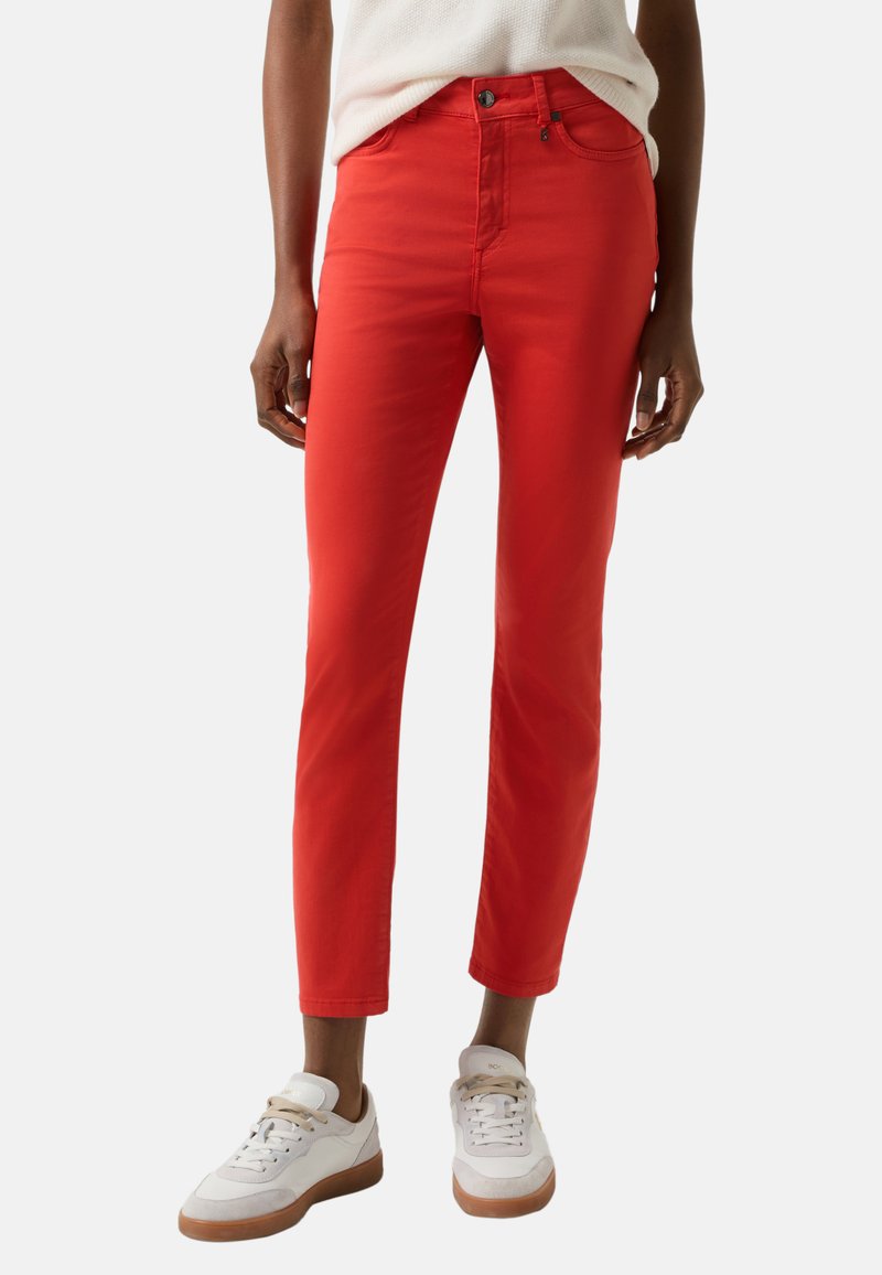 Rote Slim-Fit-Jeans aus Denim mit klassischem Fünf-Taschen-Design, Reißverschluss und Knopfverschluss, kombiniert mit weißen Sneakers.