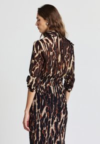 Vestito lungo stampato con vita aderente, caratterizzato da una combinazione di colori marrone, nero e beige, texture trasparente e scollo modesto con dettaglio a fiocco.