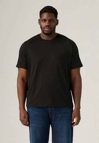 Black short-sleeve t-shirt with a crew neck, made from soft fabric. Worn with blue denim jeans, featuring a relaxed fit and minimal design.