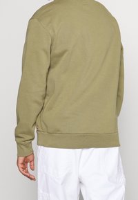 Sweat-shirt vert olive avec col rond, poignets et ourlet côtelés. Confectionné dans un matériau doux à la texture lisse. Design minimaliste, sans motifs.