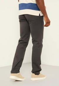 Dark gray pants with a slim fit, featuring side pockets and contrasting stitching, paired with light tan sneakers.