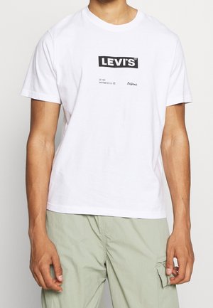 Mann trägt weißes Levi's T-Shirt mit schwarzem Logo und Text „EST 1873 SAN FRANCISCO CA California“, kombiniert mit hellgrüner Hose.