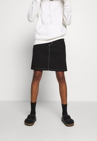 Black denim skirt with white stitching, paired with a white hooded sweatshirt, black socks, and sandals. Simple design and relaxed fit.