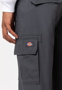 Grijze cargobroek met een gestructureerde afwerking, voorzien van een zijzak en een zichtbaar Dickies-logo op de flap.