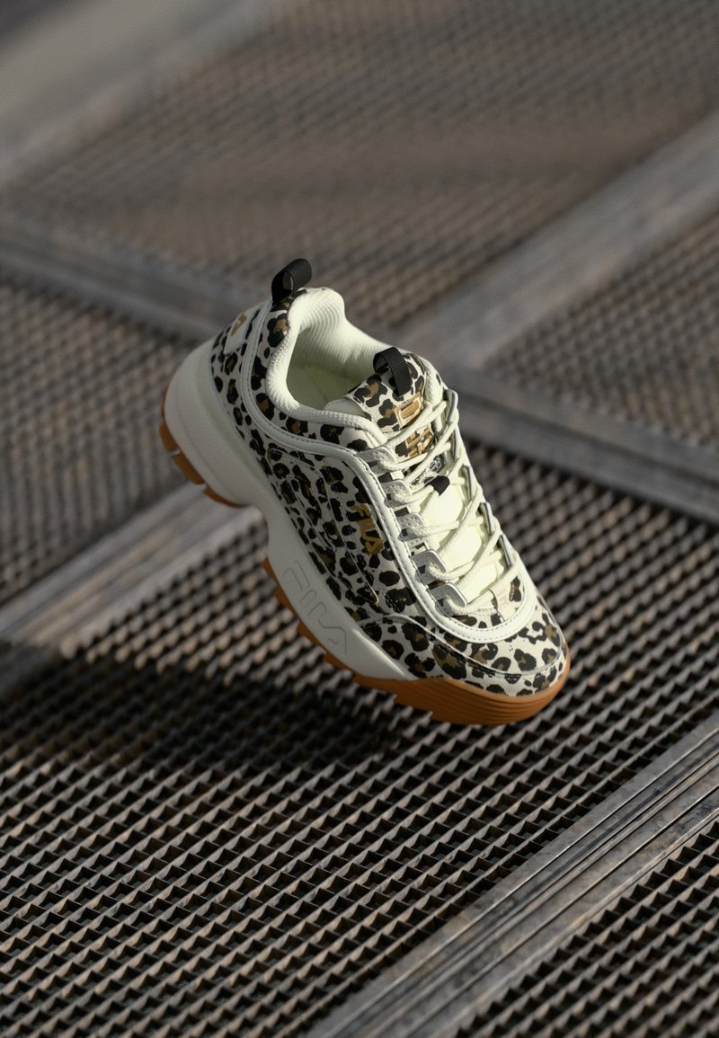 Leopard-print sneaker featuring a cream upper, textured rubber sole, and black accents. Includes intricate lacing and logo detail.
