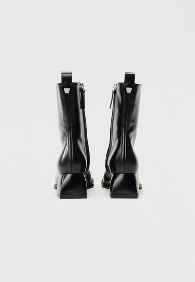 Μαύρες δερμάτινες μποτίνες μέχρι τον αστράγαλο με τετράγωνη τακούνι, διαθέτοντας λείο φινίρισμα, πίσω φερμουάρ και κατακόρυφες ραφές.