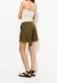 Pantaloni cargo verdi oliva con numerose tasche, in tessuto morbido e dal fit rilassato. Indossati con sandali neri con cinturino regolabile.