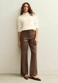 Suéter de cuello alto de lana crema, pantalones acampanados de cintura alta marrones y bailarinas marrones. Textura suave, corte casual y paleta de colores neutros.
