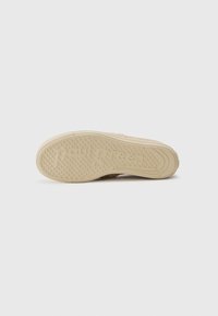 Sneaker sole in light beige with textured grip pattern. Features the brand name embossed on the side. Smooth rubber material.
