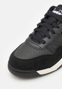Black sneaker featuring a combination of smooth leather and suede. Perforated detailing on the toe box and fitted laces. Rubber sole.