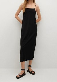 Černé midi šaty s tenkými ramínky, rovný silueta, měkká textura a mírně rozšířený lem, doplněné černými páskovými sandály.